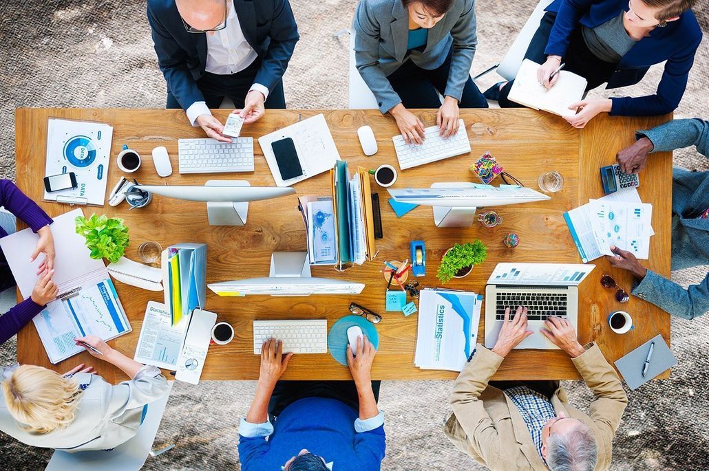 An HR team collaborating around a table covered with reports and laptops